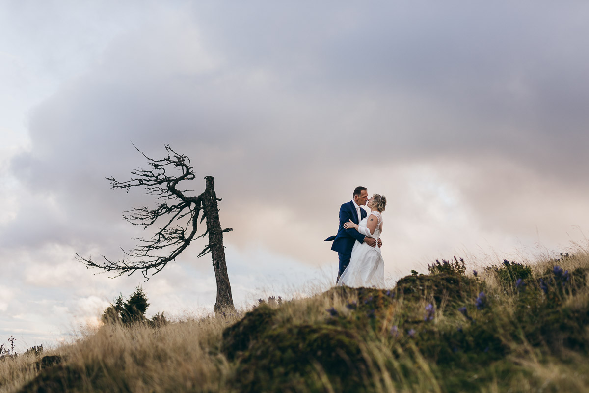 Kuss von Braut und Bräutigam vor lila Wolken beim After-Wedding-Shooting auf der Sommeralm